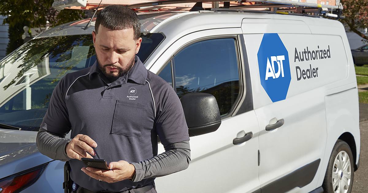 A uniformed 1 Vision USA Security representative — an ADT Authorized Dealer — beside a marked company vehicle in a neighborhood.